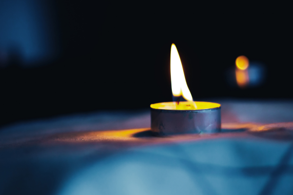 A lit tea light on a flat surface against a dark background